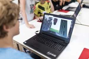Junge sitzt vor einem Laptop, auf dem eine virtuelle Welt in CoSpaces geöffnet ist