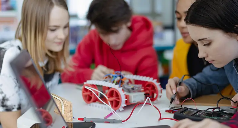 Teenager Gruppe sitz am Tisch mit einem Roboter und tüfteln an einer Platine.