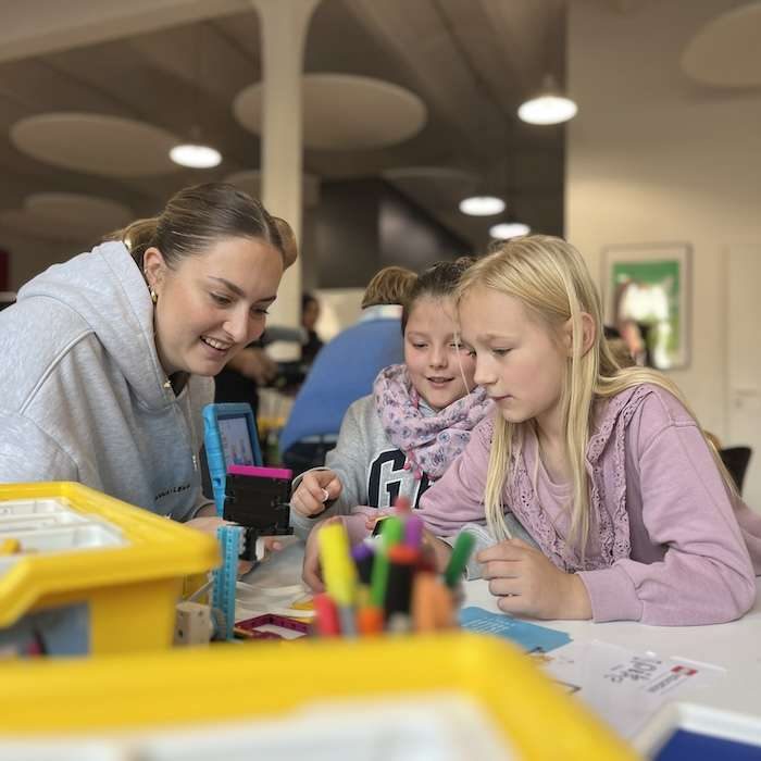 Trainerin und zwei Mädchen bauen einen Lego Roboter