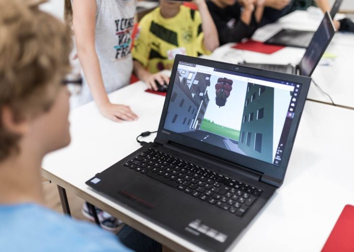 Junge sitzt vor einem Laptop, auf dem eine virtuelle Welt in CoSpaces geöffnet ist