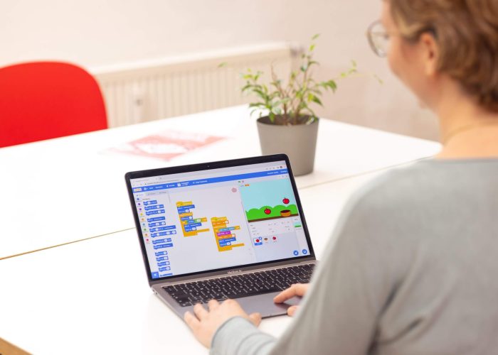 Eine Frau sitzt vor einem Laptop auf dem die Software Scratch geöffnet ist.
