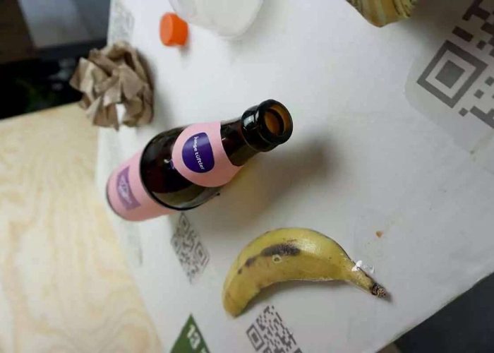 Eine Banenschale, eine Flasche, ein Deckel und ein Stück Papier liegen auf einem Tisch, daneben liegen ausgedruckte .QR-Codes