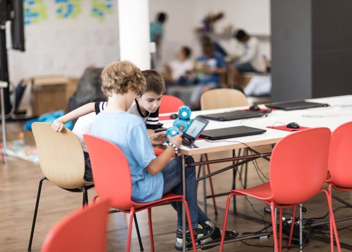 projekttag-dash-roboter Zwei Jungen sitzen an einem Tisch und betrachten einen blauen Roboter
